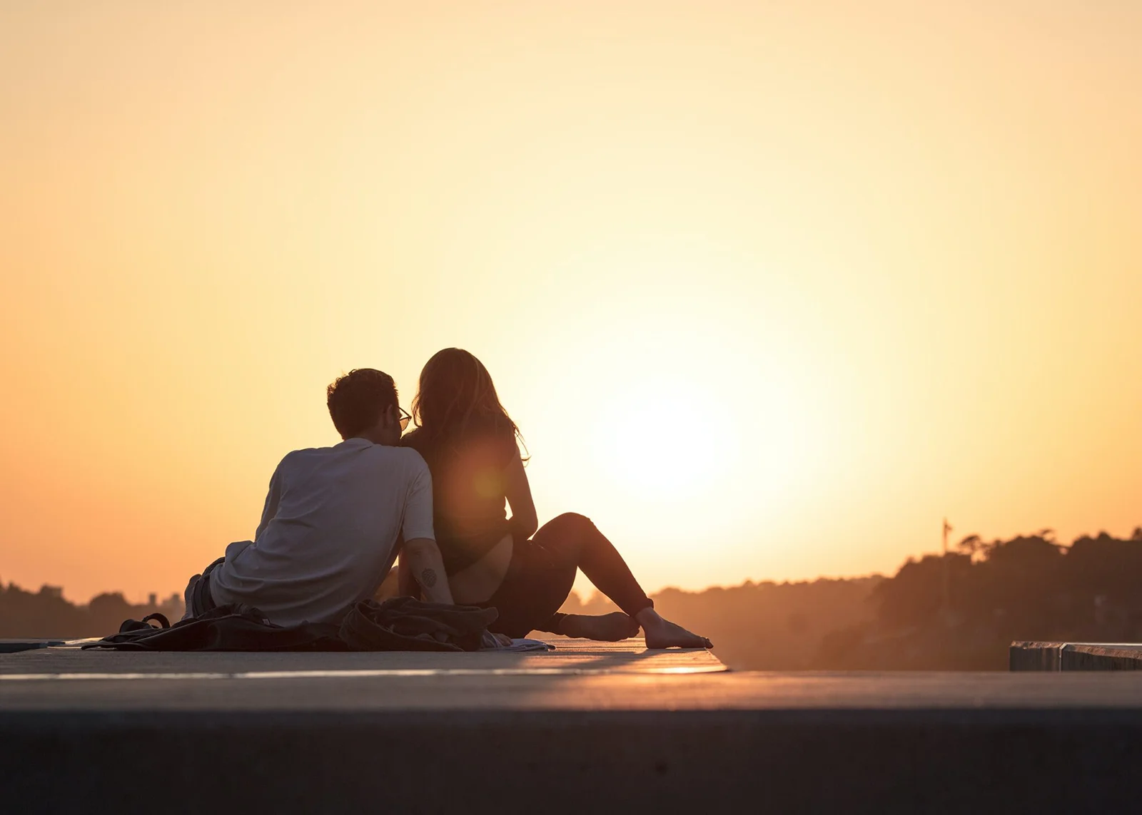 Couple sitting on roof in front of a sunset.